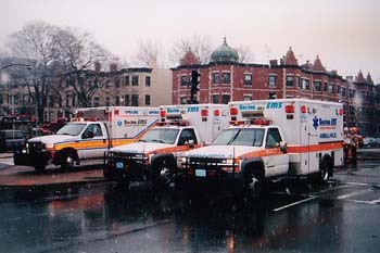 2000 Jeep Liberty - Emergency vehicles are lined up on a wet street, reflecting the overcast sky and surrounding buildings.