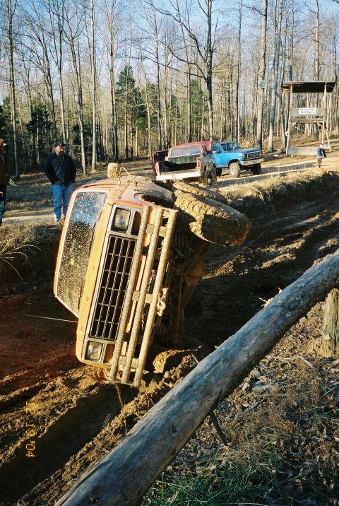 1984 Ford Bronco - An orange off-road vehicle is stuck on its side in a muddy pit with other trucks in the background.