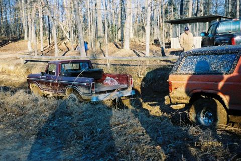 1984 Ford Bronco - A maroon 1979 Ford F-Series pickup truck is stuck in the mud, with an orange SUV attempting to pull it out of the mire.