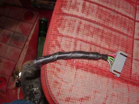 1990 Ford Bronco - Interior wiring harness with a grey connector and taped section, seen on a red patterned seat.