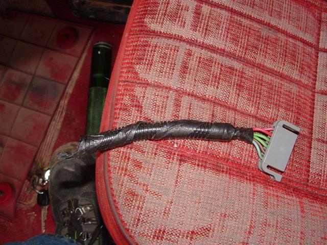 Taped wiring harness with gray multi-pin connector on a red cloth seat