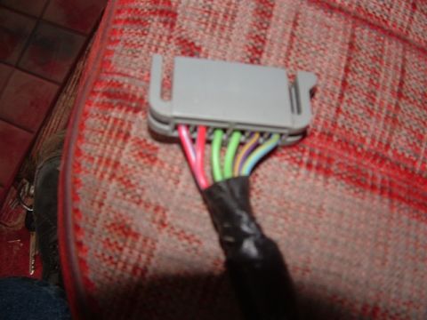1990 Ford Bronco - A close-up view of a wiring harness connector and its wires, set against the textured fabric of a vehicle's interior.