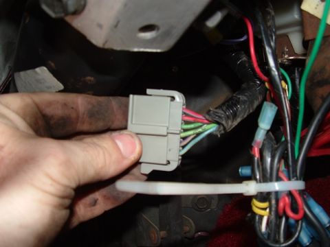1990 Ford Bronco - Close-up of a hand manipulating a vehicle's wiring harness connector, showing various colored wires and connections.