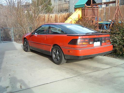 Red Ford Probe coupe parked rear-3/4 on driveway by wood fence