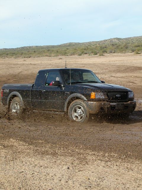 1993 Ford Bronco - A black pickup truck navigates a muddy terrain, kicking up dirt as it moves.