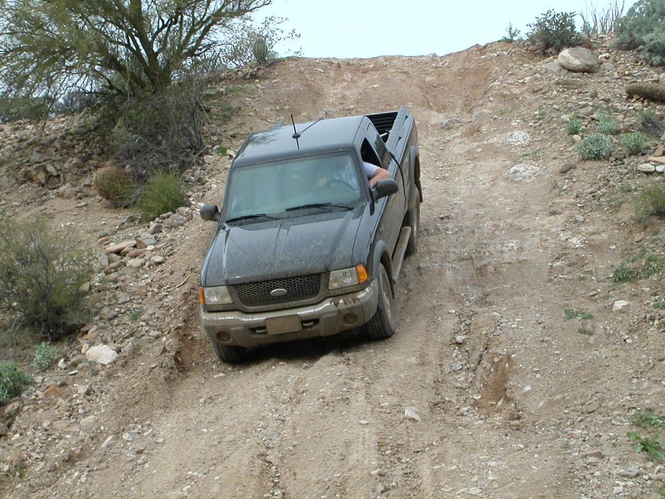 Dark gray Ford Ranger driving up a dirt hill, front 3/4 view