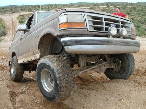 1993 Ford Bronco - A lifted 1992 Ford Bronco navigates a dusty, off-road trail with a person visible in the background.