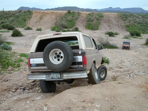 1993 Ford Bronco - This 1993 Ford Bronco is navigating a rough, dusty terrain with hills in the background.