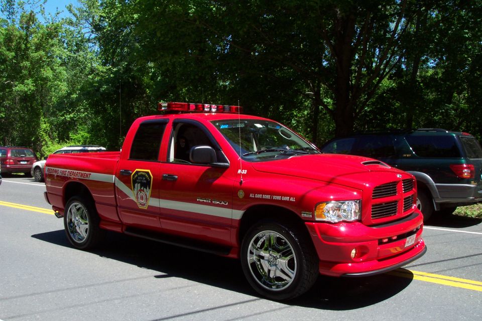 Red Dodge Ram 1500 fire department pickup with light bar and chrome wheels, 3/4 front view on a road