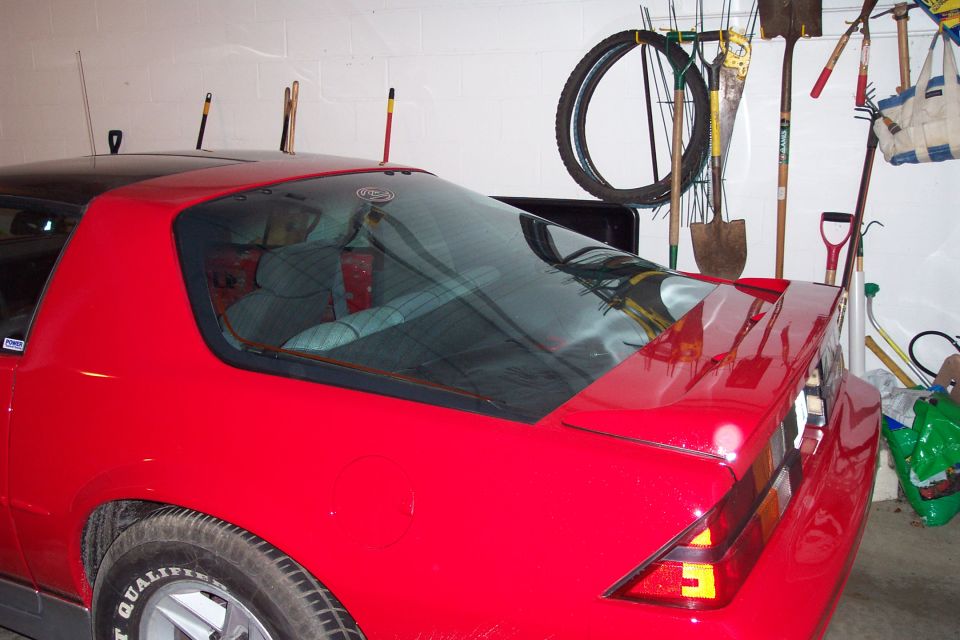 Rear quarter and hatch of red third-gen Camaro with spoiler in cluttered garage