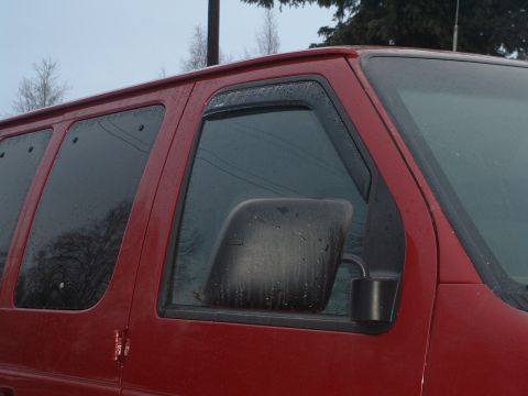 1994 Ford E350 - A red van is seen from the side, with rain droplets on the windows and a black side mirror.