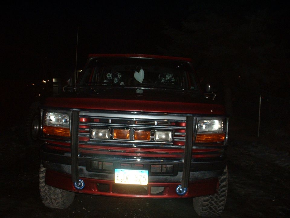 Night front view of dark red Ford pickup with chrome brush guard and yellow license plate.