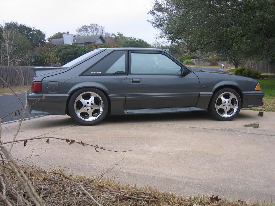 Profile of gray Fox-body Mustang GT hatchback with chrome wheels on driveway