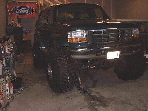1996 Ford Bronco - Green Ford Bronco with oversized tires is lifted by a jack in a garage.