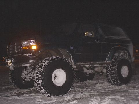 1996 Ford Bronco - A dark 1996 Ford Bronco equipped with oversized tires sits in the snow during nighttime.