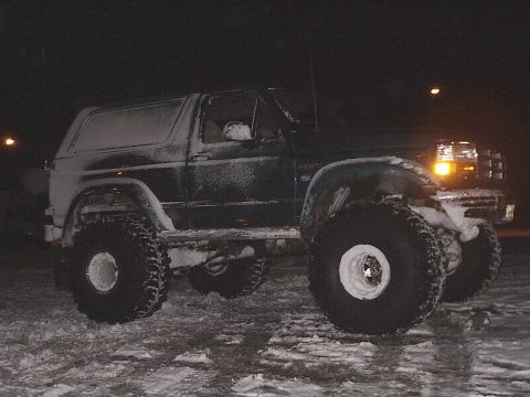 1996 Ford Bronco - Ford Bronco with large tires covered in snow, parked outside at night.