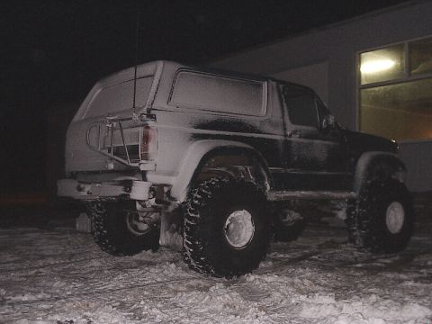 1996 Ford Bronco - A snow-covered Ford Bronco sits parked outside a building during the night.