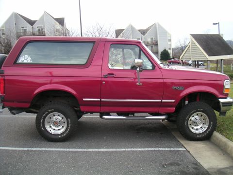 1994 Ford Bronco - A red Ford Bronco with a lifted suspension and off-road tires is parked on a curb.