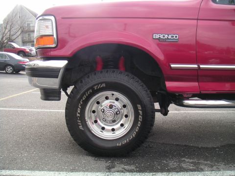 1994 Ford Bronco - Close-up of a red 1994 Ford Bronco's front fender and tire, showing aftermarket shocks.