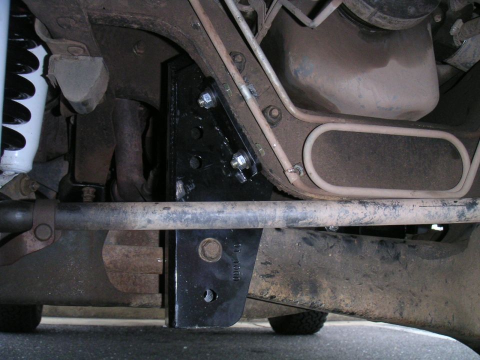 Underside view of a vehicle's suspension with a black metal bracket bolted to the frame