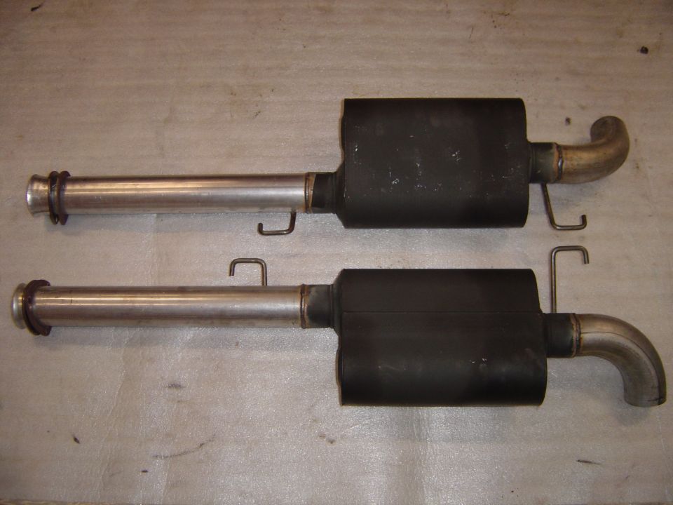 Two exhaust mufflers with stainless inlet pipes and curved tailpipes on cardboard
