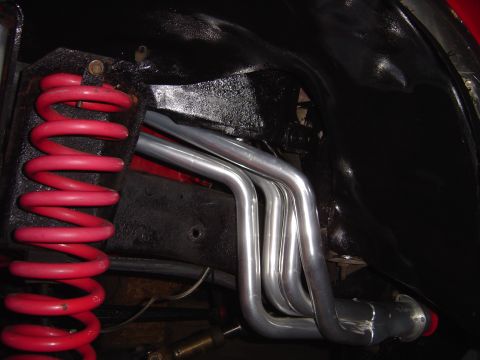 1978 Ford Bronco - Close-up view of exhaust headers and a red coil spring in the vehicle's undercarriage.