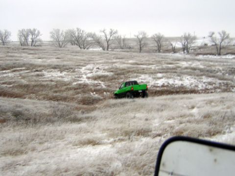 1995 Ford Bronco - A green pickup truck navigates a snow-covered field with sparse trees in the background.