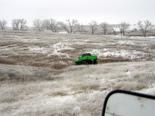 Green pickup truck driving through a snowy field