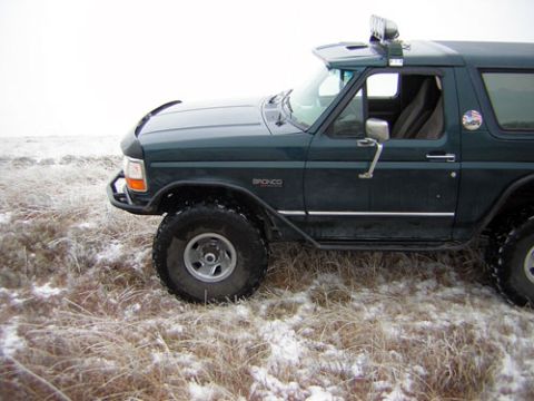 1995 Ford Bronco - 1995 Ford Bronco in a snowy field, showing its side profile and off-road modifications.