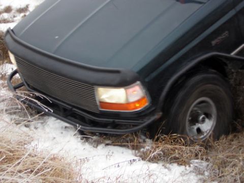 1995 Ford Bronco - Front corner of a green Ford pickup with a billet grille and tube bumper sunk into a snowy, grassy ditch.