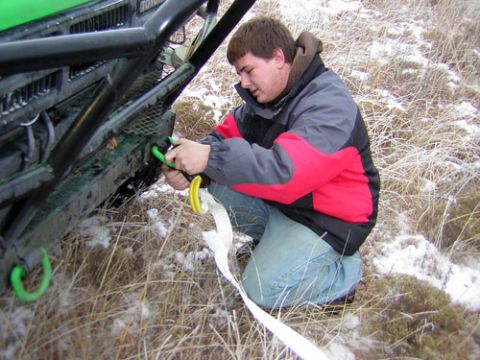 1995 Ford Bronco - A man is attaching a tow strap to the front of a green off-road vehicle in a snowy, grassy area.
