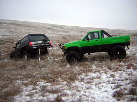 1995 Ford Bronco - A green Toyota pickup truck tows a black SUV out of a snowy, grassy field.