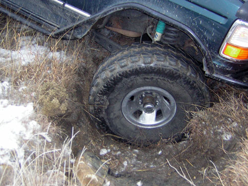 Dark green Ford SUV rear wheel stuck in a snowy ditch bank
