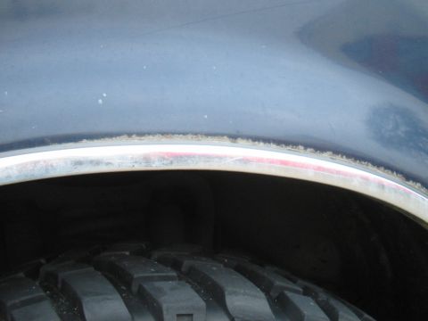 1992 Ford Bronco - Close-up of a vehicle's wheel well shows tire tread and rust on the fender trim.