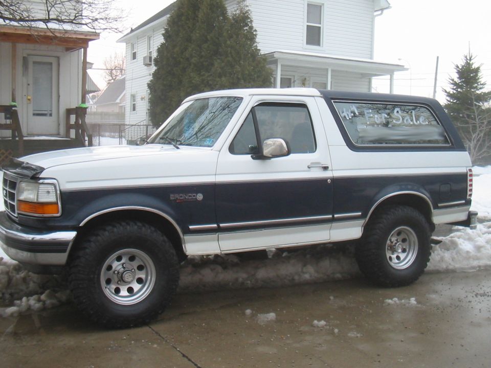 Two-tone white and dark blue Ford Bronco parked in snow, with 'For Sale' sign in window