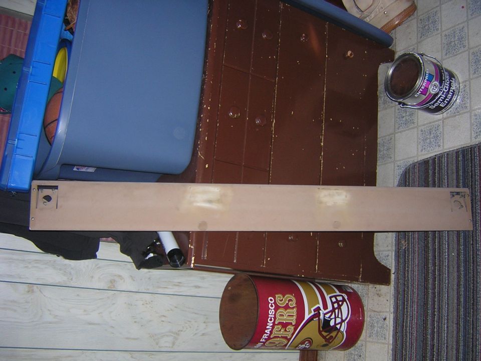 Tan panel with screw holes and a square cutout, resting on a floor