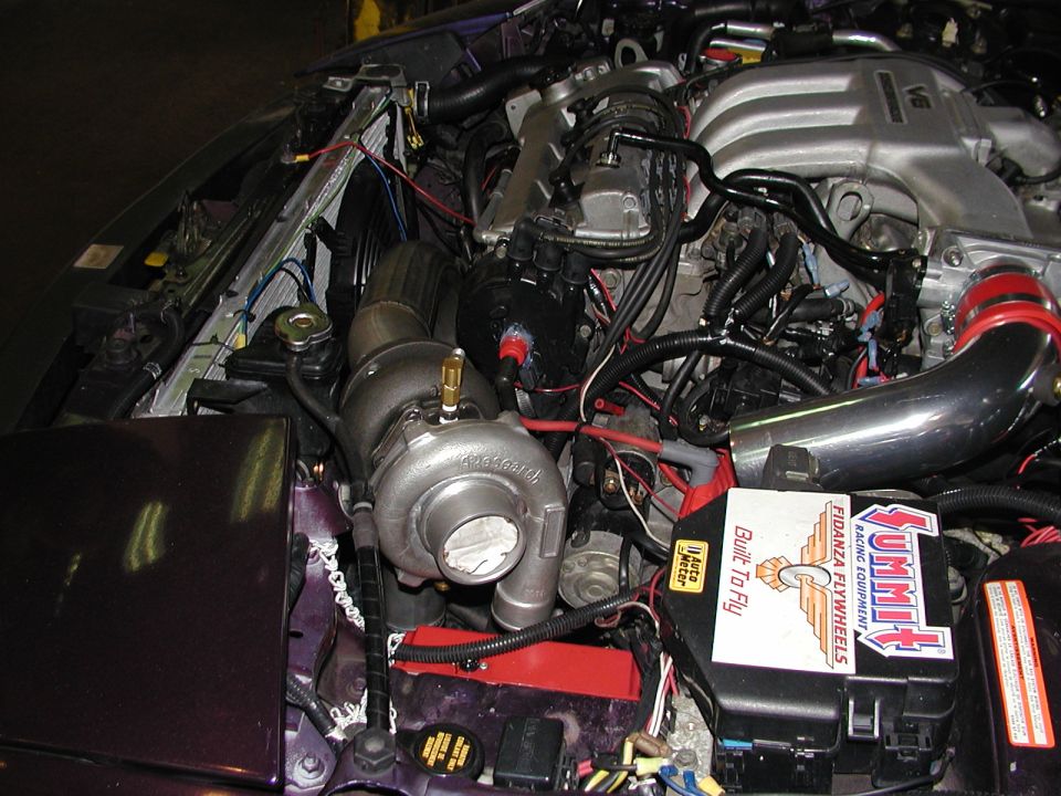 Turbocharged V6 engine bay of a purple Ford Probe with polished intake pipe and Summit Racing stickers