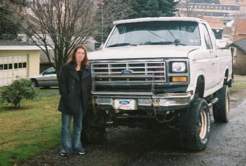 Lifted white Ford pickup parked in driveway with person standing beside the front grille.