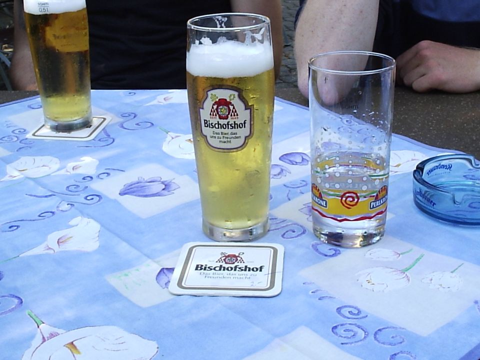Table with two glasses of beer, an empty glass, and an ashtray on a blue patterned tablecloth