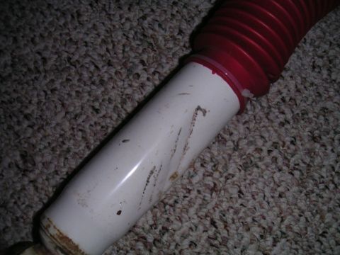 1994 Ford Bronco - A close-up view of a shock absorber with red bellows rests on a carpeted surface.