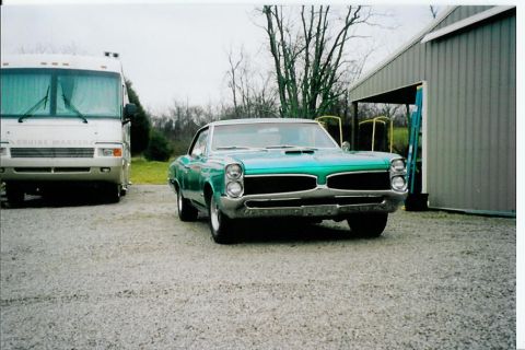 1967 Pontiac Lemans - A green 1967 Pontiac Lemans is parked in front of a building, with an RV to its left.