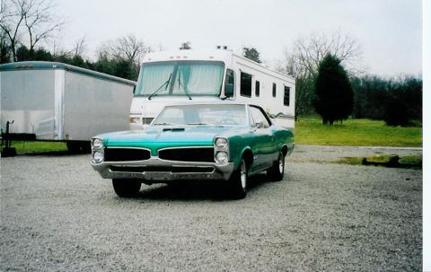 1967 Pontiac Lemans - A teal 1967 Pontiac GTO is parked on a gravel lot with an RV and trailer behind it.