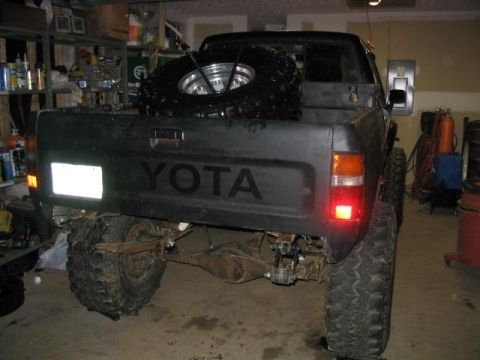 1986 Ford F-150 - Rear view of a black Toyota pickup truck, showing the tailgate with "YOTA" lettering and a spare tire mounted in the bed.