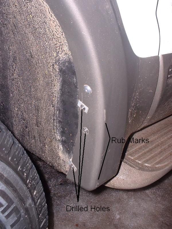 Wheel well showing drilled holes and rub marks after mud flap removal, with labels
