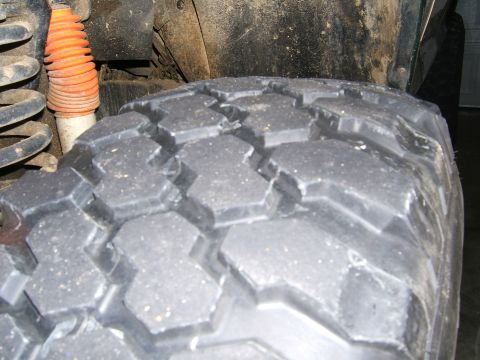 1978 Ford Bronco - A close-up view of a vehicle's tire and suspension system, showing off-road tread and an orange shock boot.