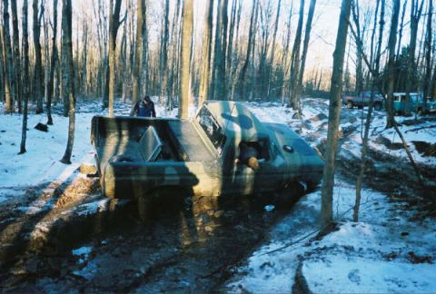 1977 Ford F-150 - A 1977 Ford F-150, camouflaged and stuck in a muddy, snowy forest, with other vehicles visible in the background.