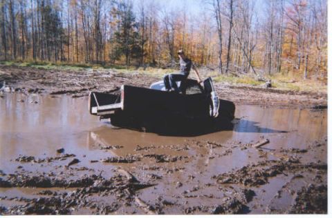 1977 Ford F-150 - A truck bed is stuck deep in a muddy area with a person sitting on top.
