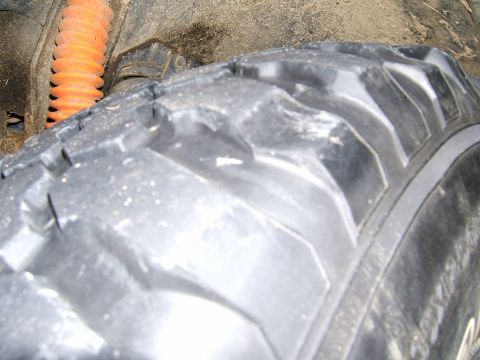 1978 Ford Bronco - A close-up view of a vehicle's tire and suspension system, showing off-road tread and an orange shock absorber.