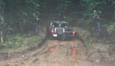 1977 Ford F-150 - A black 1977 Ford F-150 navigates a muddy off-road trail with two people standing nearby.