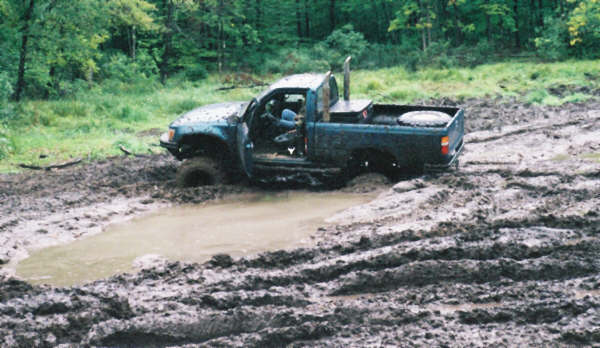 Pickup truck with door open stuck in deep mud, spare tire in bed, tall exhaust pipe